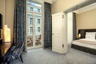 Einblicke in eine blaue Junior Suite mit kleinen Balkon und Balkonmöbel und Blick auf das Atrium