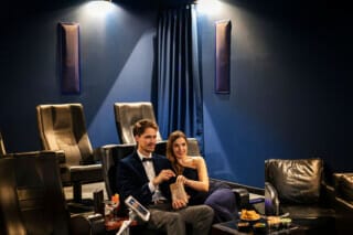 Ein privates Kino, in dem ein Pärchen mit einer Tüte Popcorn gemütlich sitzt. Das Kino kann für private Veranstaltungen gemietet werden und bietet eine exklusive und intime Atmosphäre für Filmabende oder besondere Anlässe. Die komfortablen Sitzplätze und die hochwertige Technik sorgen für ein unvergessliches Filmerlebnis.