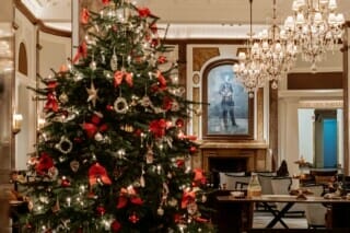 Weihnachtlich dekorierter Baum im eleganten Hotel mit Kronleuchtern und festlicher Stimmung.