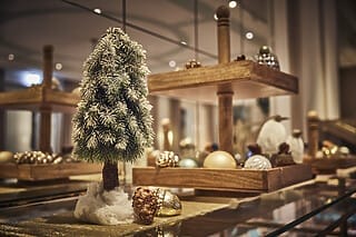 Kleiner, dekorierter Weihnachtsbaum mit Weihnachtskugeln und Tannenzapfen im Hintergrund.