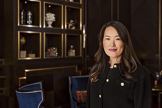 Professional woman in black sweater smiling in a stylish interior with decorative shelves.