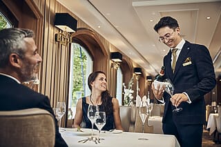 Gäste in eleganter Restaurantatmosphäre, während ein Kellner Wein serviert.