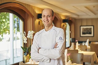 Koch in der Hotel Atlantic Küche, lächelnd mit verschränkten Armen, elegante Restaurantatmosphäre.