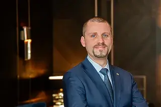 Mann in Anzug mit lächelndem Gesicht, stehend in modernem Innenraum.