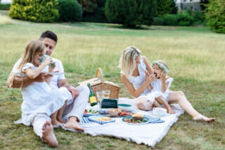 Falkenstein Grand Eine fröhliche Familie, die auf einer Picknickdecke im Park sitzt.
