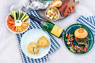 Falkenstein Grand Picknickdecke im Park mit Antipasti, Gemüsesticks mit Quark, feinem Bulgur-Salat und Brioche-Bun-Beef-Burger.