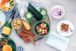 Falkenstein Grand Eine Picknickdecke mit Trauben, Fruchtjoghurt mit Beeren und Erdbeeren, Antipasti und Gemüsesticks, ausgebreitet für ein leckeres Picknick im Freien.