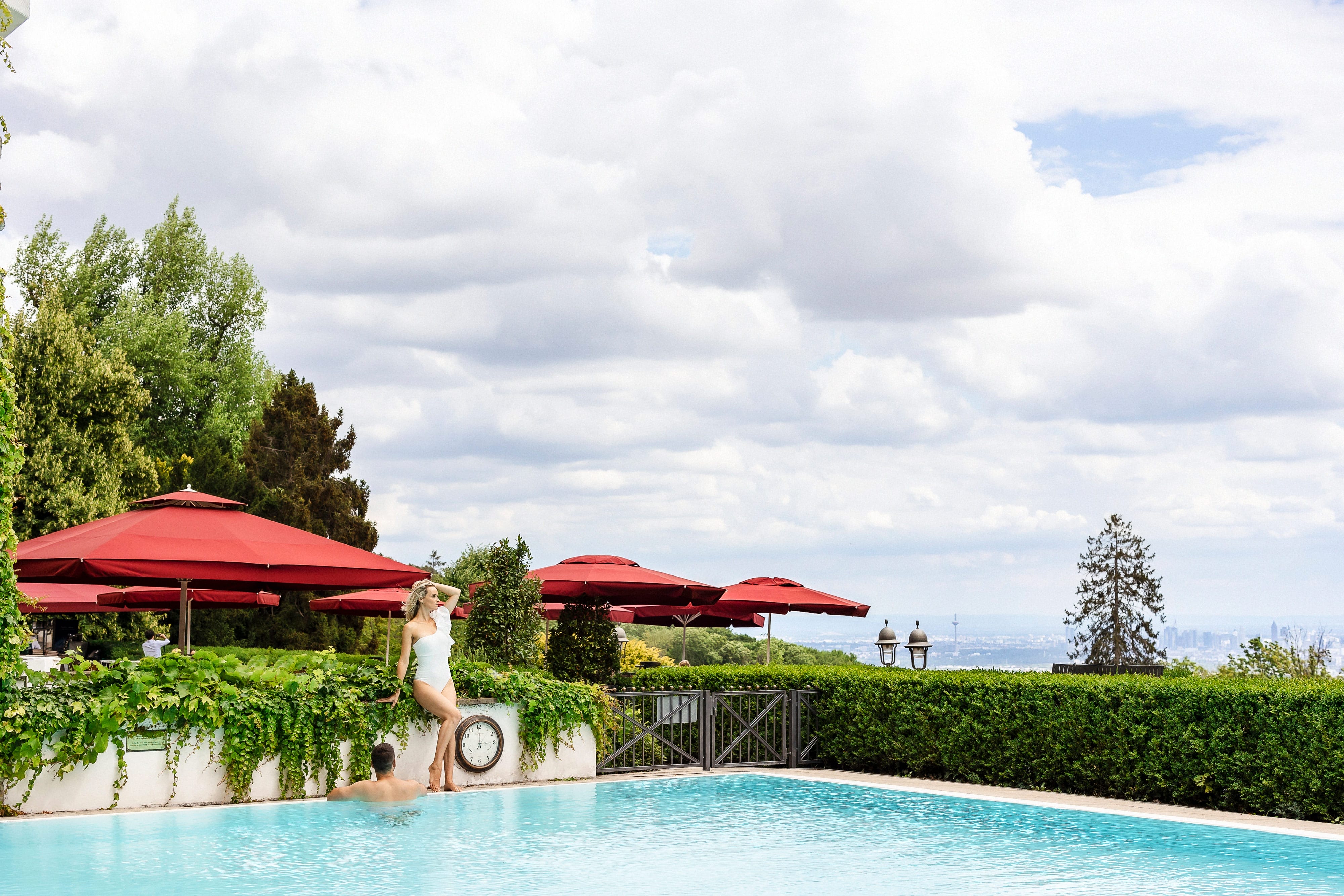 Falkenstein Grand Ein Pool neben einem Picknick im Park mit Blick auf die Skyline von Frankfurt. Ein Mann und eine Frau genießen den Tag im Freien.